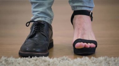 Kafkas erkek ayaklarının son derece yakın plan çekimleri. Bir bacağı erkek çizmesinde, diğeri kadın yüksek topuklu ayakkabısında. Cinsiyetler arası insanlar, ikili cinsiyet.