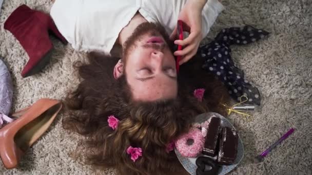 Camera moving around face of positive Caucasian intersex person talking and hanging up phone. Top view portrait of binary gender man with makeup on face and flowers in hair. — Stock Video