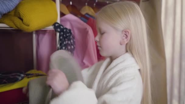 Close-up side view of Caucasian girl putting on hat and eyeglasses. Portrait of little cute kid trying on clothes indoors. Elegance, fashion, joy. — Stock Video