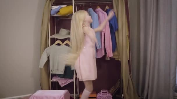 Blond blank meisje in roze jurk springen en spinnen in de voorkant van de garderobe thuis. Vrolijk mooi kind heeft plezier in het weekend binnen. Vreugde, levensstijl, kindertijd. — Stockvideo