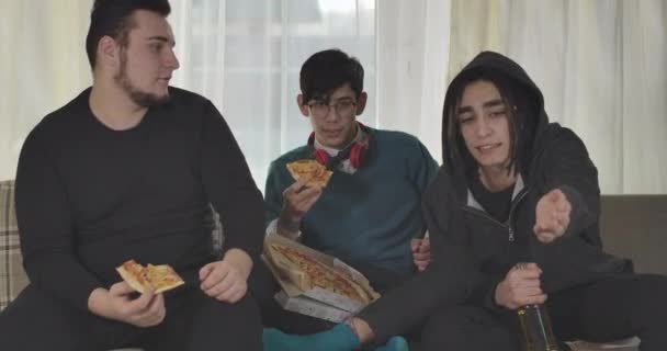 Tre vita bästa vänner äter pizza och dricker öl inomhus. Vuxna studenter sitter på soffan och tittar på matchen på Tv. Glada fotbollsfans tittar på deras lag vinna. Cinema 4k Prores Hq. — Stockvideo