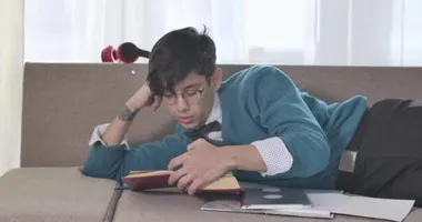 Kitap okuyan ve esneyen yorgun beyaz adamın portresi. Gözlüklü yorgun üniversite öğrencisi, kanepede uzanıyor gibi uyuyor. Sinema 4k Prores Merkezi.