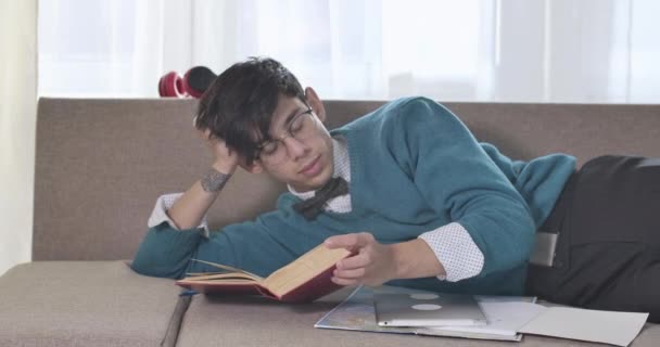 Giovane ragazzo caucasico stanco in occhiali con tatuaggio a portata di mano addormentarsi al chiuso. Studente universitario maschio esausto che studia a casa sul divano. Cinema 4k ProRes HQ . — Video Stock