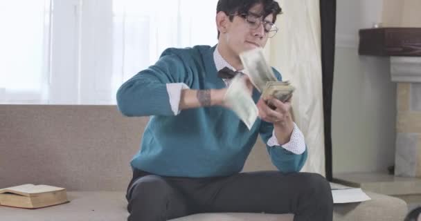 Sonriente hombre caucásico con gafas y pajarita esparciendo y vomitando dinero. Un chico rico seguro disfrutando de una vida rica. Riqueza, estilo de vida, alegría. Sede del cine 4k ProRes . — Vídeos de Stock