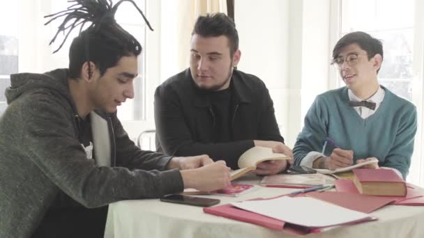 Drie jonge blanke mannen zitten aan tafel, pratend en lachend. Studenten van de mannelijke universiteit studeren samen binnen. Vrienden die graag studeren. Onderwijsconcept. — Stockvideo