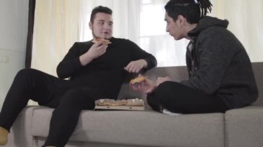 İki beyaz erkek arkadaş pizza yiyip sohbet ediyorlar. Yetişkin üniversite öğrencileri hafta sonları evde dinleniyor. Boş zaman, yaşam tarzı, iletişim..