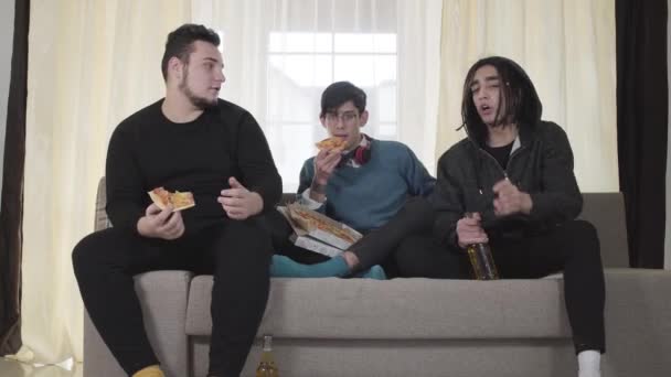 Portrait of three Caucasian best friends watching football match, eating pizza and drinking beer. Young enthusiastic fans gesturing and discussing TV show, showing victory gesture. — 비디오