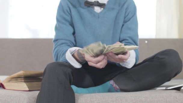 Detailní záběr mužských bělošských rukou s tetováním počítání peněz. Šťastný mladý muž se opřel o gauč a držel dolary na prsou. Bohatství, bohatství, životní styl. Zaměřeno na popředí. — Stock video