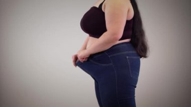 Şişman, beyaz kadın, esnek kot pantolon giyiyor. Şişman, genç, tanınmayan bir kız içeride giyiniyor. Aşırı kilolu, obezite, selülit.