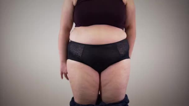Joven mujer gorda caucásica poniéndose jeans. Retrato de chica regordeta vistiéndose. Mujer obesa con celulitis que tiene problemas de sobrepeso . — Vídeos de Stock