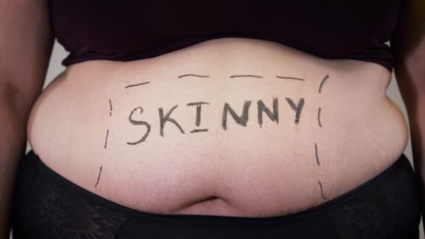 Primo piano della pancia caucasica femminile con scritta la parola Skinny. Pancia di giovane donna obesa. Sovrappeso, obesità . — Video Stock