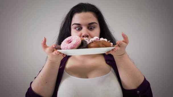 Porträtt av hungrig vit fet kvinna som tar tallrik med sötsaker och luktar dessert. Överviktiga flicka tittar girigt på mat. Kameran närmar sig ansikte mot ansikte. Ohälsosamt ätande, fetma. — Stockvideo