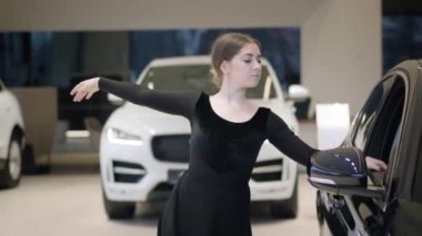 Araba galerisinde dans eden güzel beyaz kadın portresi. Otomobil galerisinde ince balerin performansı. Siyah aracın yanında bayan balerin. Yaşam tarzı, araba işi, dans..
