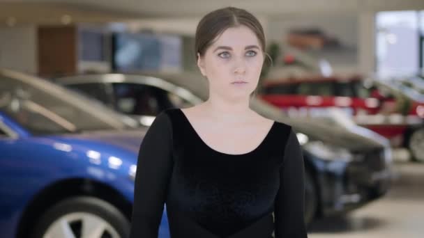 Primo piano di bruna donna caucasica piegatura e filatura in concessionaria auto. Giovane ballerina fiduciosa che balla nello showroom di auto. Industria automobilistica, eleganza, arte . — Video Stock