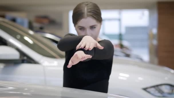 Zelfverzekerde blanke ballerina dansend in de autohandel. Vrouwelijke balletdanser beweegt tussen witte auto 's in de showroom. Auto-industrie, kunst, schoonheid. — Stockvideo