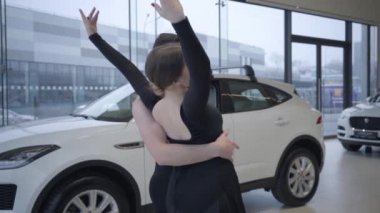 Slowmo of smiling Caucasian woman bending back supported by man. Happy ballet dancers dancing in car dealership. Auto industry, elegance, art, beauty. Slow motion.