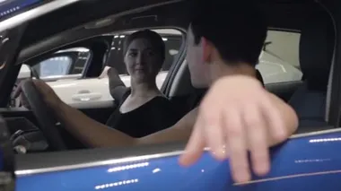 Kamera sağdan sola hareket ediyor. Gülümseyen beyaz bir adam ve kadın arabada oturuyor. Araba galerisinde poz veren zarif erkek ve kadın balerinler. Otomobil endüstrisi, zarafet, güzellik. Yavaşla.