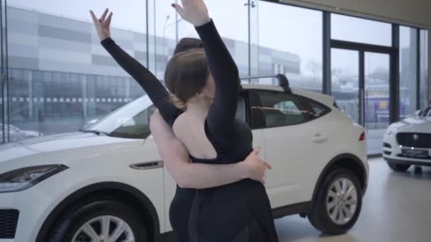Повільне посміхаючись, кавказька жінка згинається, підтримувана чоловіком. Щасливі танцюристи балету танцюють в автосалоні. Автомобільна промисловість, елегантність, мистецтво, краса. Повільний рух. — стокове відео
