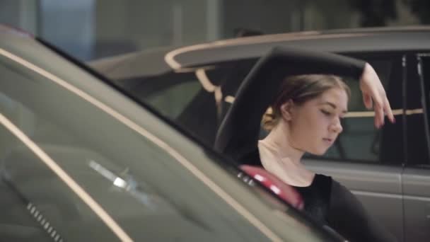 Câmara lenta, dançarina de ballet caucasiana a curvar-se na concessionária de carros. Bela dança profissional entre carros. Arte, graça, elegância, indústria automobilística. Devagar. . — Vídeo de Stock