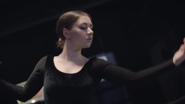 Portrait of female Caucasian ballet dancer moving hands up and down. Beautiful young woman dancing in darkness. Art, lifestyle, elegance. Slowmo. — Stock Video