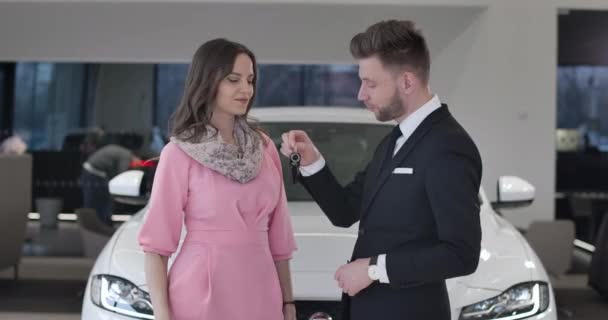 Caucasian car dealer giving keys to beautiful young businesswoman and shaking clients hand. Happy successful lady buying new automobile in car dealership. Cinema 4k ProRes HQ. — Stock Video