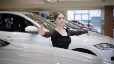 Otomobil galerisinde beyaz arabaların arasında parmak uçlarında dönen kendine güvenen beyaz kadın. Araba galerisinde pratik yapan güzel bir bayan balerin. Zarafet, sanat, yaşam tarzı.