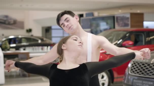 Bailarines de ballet caucásicos profesionales doblando y girando en la sala de exposición de automóviles. Hombre y mujer bailando sensual danza clásica en concesionario de coches. Industria automotriz, elegancia, arte . — Vídeos de Stock