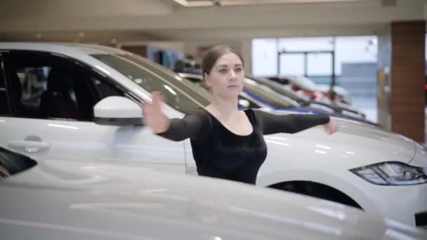 Mujer caucásica confiada girando de puntillas entre coches blancos en la sala de exposición de automóviles. Hermosa bailarina de ballet practicando en concesionaria de autos. Elegancia, arte, estilo de vida . — Vídeos de Stock