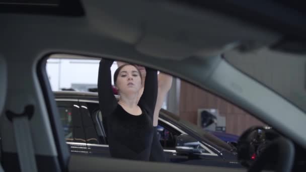 Two young Caucasian dancers spinning and looking at camera. Man and woman dancing ballet dance in car dealership. Shooting from automobile salon, slow motion. Performance, art, elegance. — 비디오