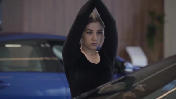 Retrato de la elegante mujer caucásica moviendo lentamente las manos hacia abajo. Bailarina de ballet femenina bailando en la sala de exposición de autos. Estilo de vida, elegancia, arte. Movimiento lento . — Vídeos de Stock