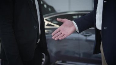 Tanımlanamayan iki beyaz adamın araba galerisinde otomobillerin önünde el sıkışması. Satıcı ve müşterinin el sıkışması. Otomobil işi, otomobil endüstrisi..