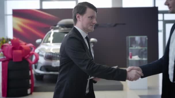 Retrato de sorridente carro caucasiano revendedor acolhedor cliente no showroom. Empresário bem sucedido entrando na concessionária de automóveis para comprar um novo veículo. Indústria automobilística, negócios, reunião . — Vídeo de Stock