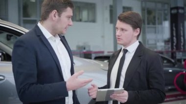 Kafkasyalı esmer araba satıcısı tablet kullanarak müşteriye özelliklerini gösteriyor. Satış temsilcisi müşteriyle otomobil alışverişini tartışıyor. Galeri, galeri, iş yeri..
