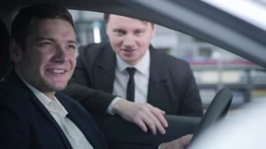 Yakışıklı beyaz adamın portresi araba kuaföründe oturuyor ve karısı ve satıcısıyla konuşuyor. Gülümseyen adam ailesine galeriden yeni bir araç alıyor. İş, başarı, otomobil endüstrisi.