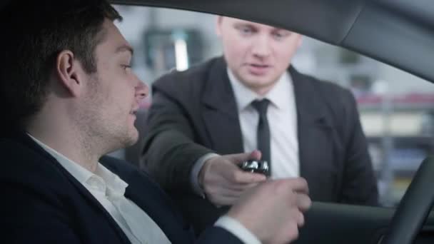 Close-up side view of confident Caucasian man taking car keys from dealer and starting engine. Portrait of happy automobile owner inside new vehicle. Automobile industry, business, success. — Stock Video