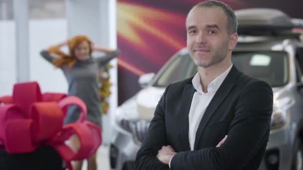 Portrait d'un homme caucasien adulte regardant en arrière la femme rousse heureuse, se tournant vers la caméra et souriant. Homme d'affaires positif achetant une nouvelle voiture pour son conjoint. Succès, mode de vie, affaires . — Video