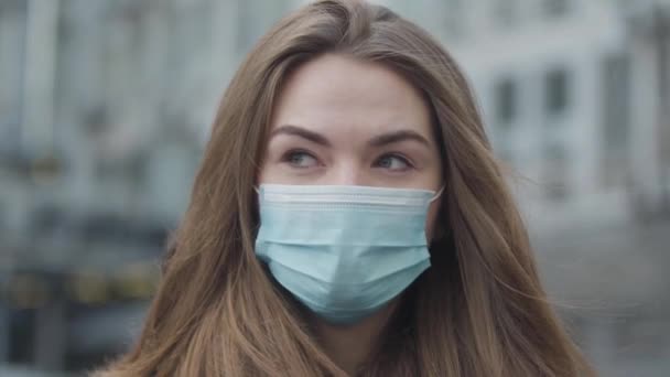 Portret van een jonge brunette die op straat rondkijkt. Close-up van mooie vrouwen gezicht in beschermend masker. Coronavirus, gevaar, gevaar, wereldwijd probleem. — Stockvideo