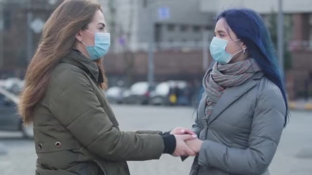 Zbliżenie dwóch młodych kobiet w maskach ochronnych stojących na ulicy i mówiących. Brunetka i jej przyjaciółka z niebieskimi włosami rozmawiają o wirusie. Niebezpieczeństwo, epidemia. — Wideo stockowe