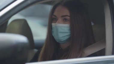 Şoför koltuğunda oturan ve koruyucu maske takan genç bir kadının yakın çekimi. Hastalık belirtileri gösteren esmer kadının portresi. Sağlık, ilaç, salgın hastalıklar.