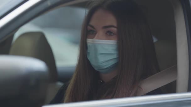 Close-up of coughing young woman sitting on drivers seat wearing protective mask. Portrait of tired brunette woman with illness symptoms. Healthcare, medicine, pandemic. — Stock Video