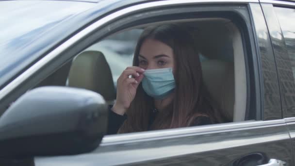 Mujer morena joven poniéndose una máscara protectora, cerrando la ventana lateral y saliendo del coche. Retrato de una mujer ansiosa protegiéndose contra el virus global. Medicina, coronavirus, peligro . — Vídeo de stock