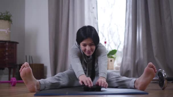 Portret van een vrolijke blanke brunette die voorover buigt op een yogamat en snoep neemt. Een glimlachende jonge vrouw die zichzelf motiveert om thuis te sporten. Lifestyle, geluk. — Stockvideo