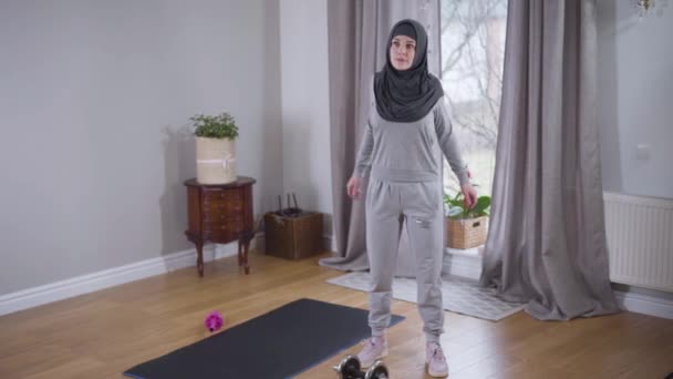 Joven mujer musulmana fuerte haciendo ejercicio en casa por la mañana. Mujer hermosa delgada en hijab practicando deporte en interiores. Salud, belleza, estilo de vida . — Vídeos de Stock