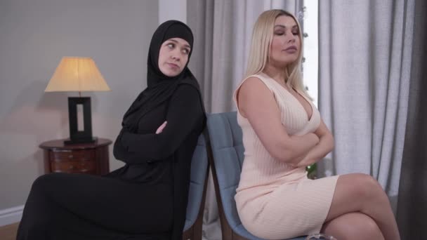 Deux femmes s'assoient dos à dos et se regardent. Dames musulmanes et caucasiennes représentant la différence culturelle. Diversité, tolérance, mode de vie, société moderne . — Video