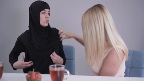 Modeste femme musulmane en hijab parlant avec un ami blond caucasien critiquant sa tenue. Dame conservatrice et fille moderne discutant des différences culturelles. Tolérance, communication, mode de vie . — Video