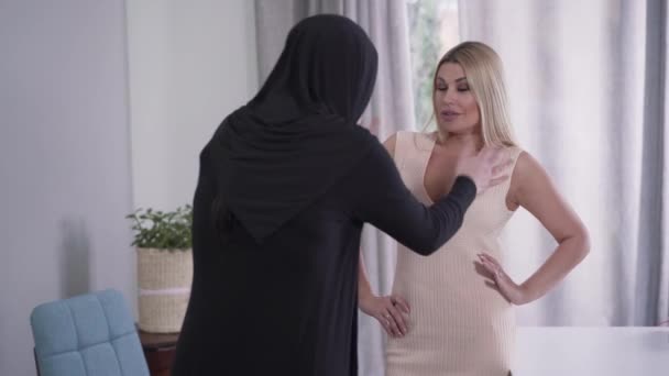 Vue arrière de musulmane modeste femme argumentant avec dame caucasienne concernant tenue. Fille conservatrice de l'Est en hijab et femme moderne en robe franche parlant à l'intérieur. Tolérance, différence culturelle . — Video