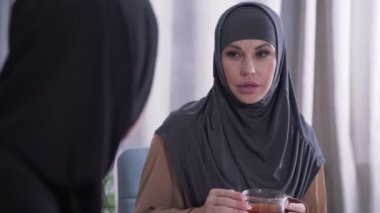 Modern Müslüman kadının tesettürlü portresi tanınmayan bir arkadaşı dinliyor. Şaşırmış genç bir bayan elleriyle ağzını kapatıp başını sallıyor. İletişim, arkadaşlık..