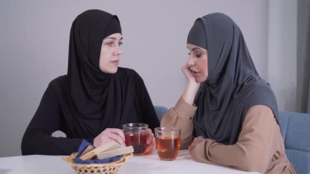 Bescheiden moslimvrouw in hijab die haar modern ogende vriendin kalmeert. Jongedame troostende en knuffelende huilende vriend. Vriendschap, communicatie, ondersteuning. — Stockvideo