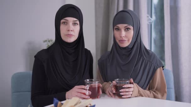 Porträtt av två självsäkra kvinnor i hijabs tittar på kameran och ler. Måttliga och moderna damer poserar inomhus. Stil, skönhet, livsstil. — Stockvideo