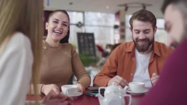 Happy young Caucasian couple talking with friends in restaurant. Cheerful man and woman resting in cafe with fellows. Youth, lifestyle, joy, happiness.